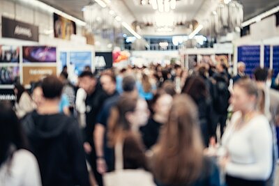 Bildungsmesse 2024 Abstraktes, verschwommenes Bild einer Messehalle und vielen Besucherinnen und Besuchern.
