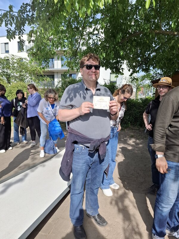 Herr Daske trägt eine dunkle Sonnenbrille und zeigt stolz seine Siegerurkunde im Minigolf in die Kamera.