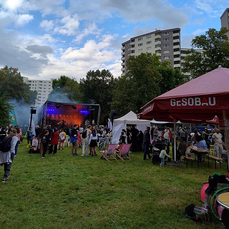 Blick auf die Festwiese, auf der viele Informationsstände stehen, zumeist überdeckt und vor regen geschützt, Besucherinnen und Besucher informieren sich über die Bildungsangebote. 