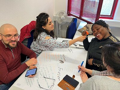 Erfolgreiche Gruppenarbeit im Berufssprachkurs Ein Mann und drei Frauen gestalten gemeinsam ein Plakat.