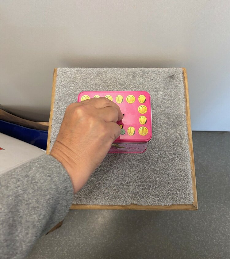 Unser Nachhaltigkeitsbasar ist immer ein Highlight Eine Hand wirft eine Münze in die rosafarbene Spendenbox aus Metall.