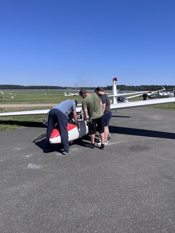 Mehrere Personen stehen an einem Segelflugzeug und schauen gemeinsam in den geöffneten Cockpitbereich.