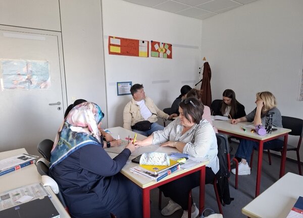 Weibliche und männliche Teilnehmende des B2-Kurses sitzen im Unterricht an Tischen und arbeiten an ihren Präsentationen.