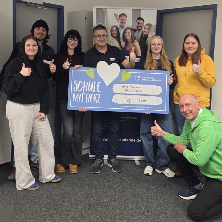 Leiter Uwe Schöneck ist umringt von seinen Auszubildenden, Herr Köhler in der Hocke mit Daumen nach oben, und hält einen übergroßen Scheck über 400 Euro ins Bild.