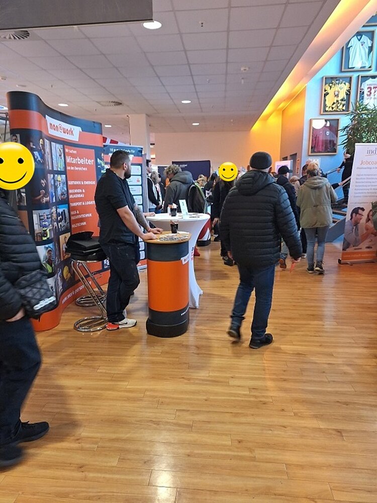 Blick in die Messehalle, mit Informationsständen und Besucher*innen.