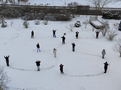 Sicht von oben auf einen schneebedeckten Platz, auf dem Schüler die Zahl 35 in den Schnee geschrieben haben; die Schüler stehen dabei und winken.