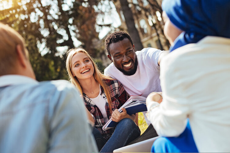 Ein Mann und eine Frau mit Heften in der Hand unterhalten sich lächelnd mit zwei ihnen gegenübersitzenden Personen.