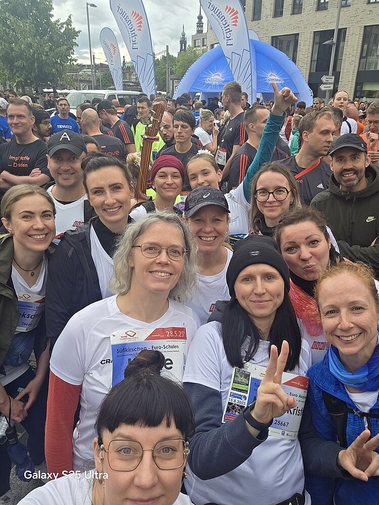 Euro-Schulen & Euro Akademie bei der Rewe Team Challenge 2025 Selfie aus der Menschenmenge kurz vor dem Start. Die Teilnehmenden lachen in die Kamera, im Hintergrund sieht man blaue Zelte der Veranstaltung und viele weitere Läufer.