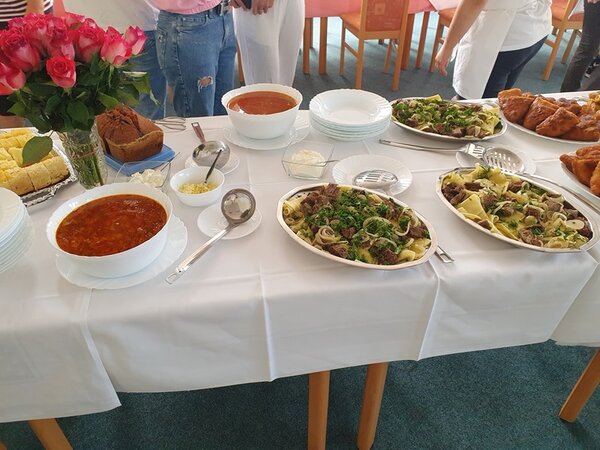 Die gedeckte Tafel, voller Köstlichkeiten und einem großen Strauß frischer Rosen in einer Vase.