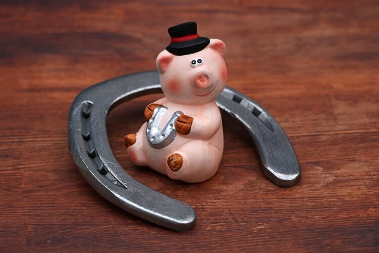 Foto von der Figur eines Glückschweines mit Hut, das ein kleines Hufeisen hält und in einem größeren Hufeisen sitzt