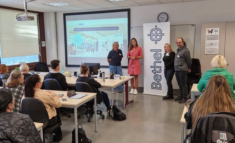 In einem Klassenraum sitzen viele Schülerinnen und Schüler die einer Präsentation zuhören.