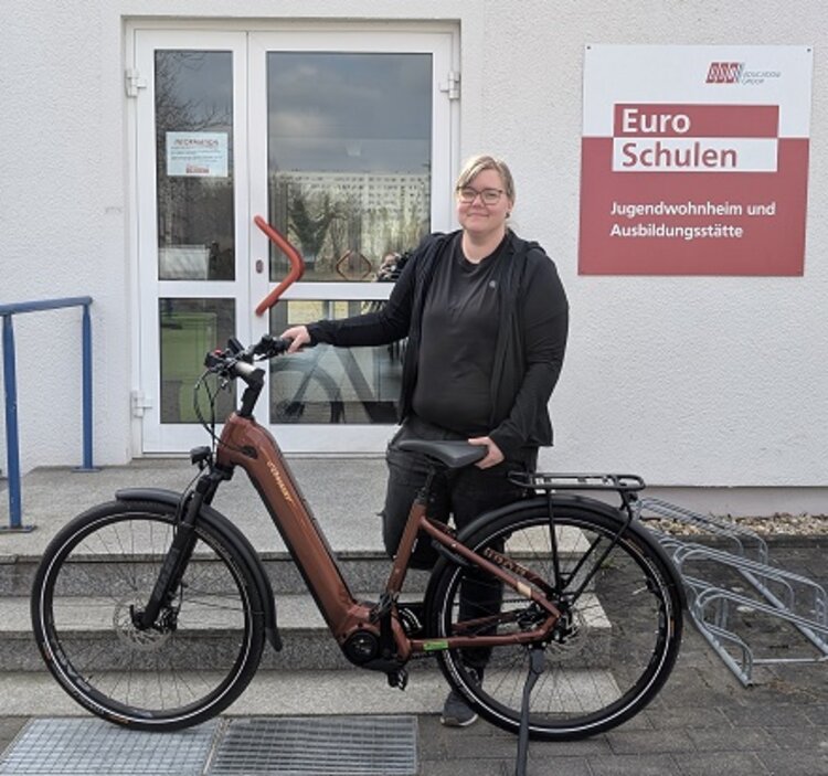 Mitarbeiterin Lisa posiert vor dem Eingang der Euro-Schulen Hoyerswerda mit ihrem neuen Fahrrad.