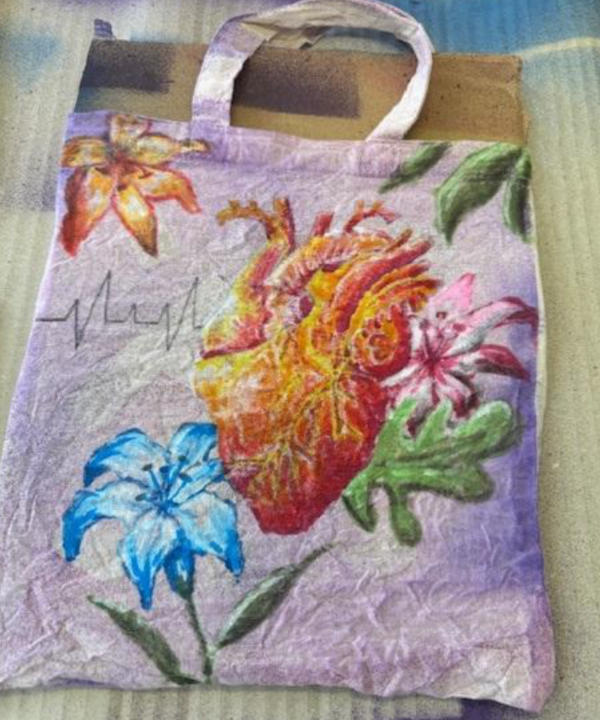 Fertig gestalteter Stoffbeutel mit großem anatomischem Herz, bunten Blumen und einer stilisierten Herzschlaglinie auf violettem Hintergrund.
