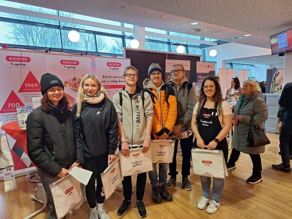 Die Teilnehmenden stehen mit Tüten mit Werbegeschenken gut gelaunt in den Räumen der Jobmesse und posieren für ein Gruppenbild.
