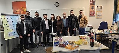 Weihnachtsfeiern in Köln Die Kursteilnehmenden stehen im Klassenzimmer und präsentieren die mitgebrachten Köstlichkeiten.nzimmer und lächeln in die Kamera.