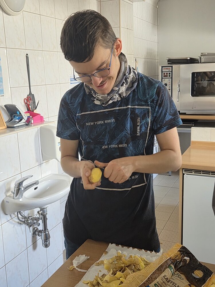 Herbstliche Köstlichkeit Ein Schüler schält mit einem kleinen Messer eine Kartoffel. Vor ihm auf der Arbeitsplatte liegt die Schalen der bereits geschälten Kartoffeln sowie Sack neuer der Marke Rewe Bio.