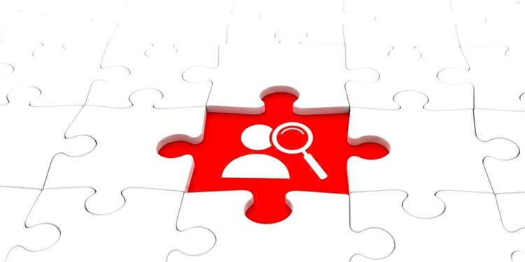 Ein einzelnes rotes Puzzlestück hebt sich aus einer Fläche weißer Puzzleteile hervor. Auf dem roten Puzzlestück ist ein weißes Symbol zu sehen: eine stilisierte Person und eine Lupe, die auf den Kopf der Person gerichtet ist.