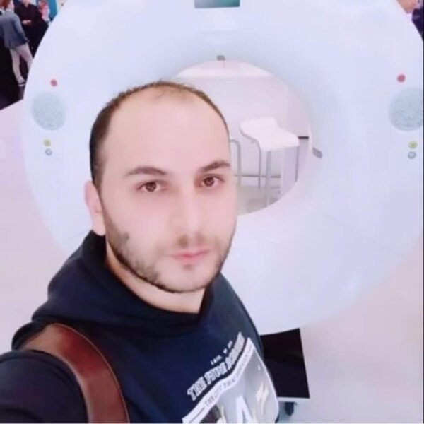 Ein Mann macht ein Selfie vor einem großen medizinischen Scanner. Im Hintergrund ist die runde Öffnung des Untersuchungsgeräts zu sehen.
