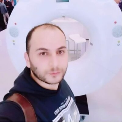 Ein Mann macht ein Selfie vor einem großen medizinischen Scanner. Im Hintergrund ist die runde Öffnung des Untersuchungsgeräts zu sehen.