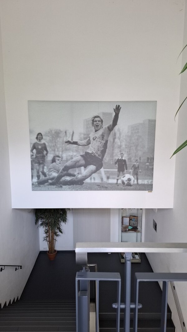 Großes Schwarz-Weiß-Bild eines legendären Fußballmoments ziert das Treppenhaus des Stadions – eine Szene voller Dynamik und Geschichte.