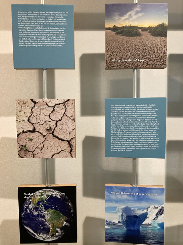 Eine Wandinstallation mit mehreren Informationstafeln und Bildern, die sich mit verschiedenen Aspekten des Wasserkreislaufs und der Wasserknappheit beschäftigen. Die Texte erklären Themen wie Verdunstung, die Veränderung der Wassermenge auf der Erde und die Bedeutung von Süßwasser.