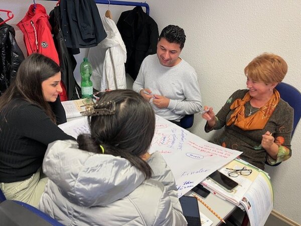 Vier Teilnehmende eines Berufssprachkurses lachen bei der gemeinsamen Arbeit.