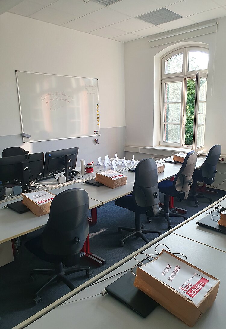 Maßnahme BaE kooperativ in Minden gestartet Zu sehen in Reihe gestellte Tische mit blauen Stühlen, auf denen Werbematerial der Euro-Schulen und Schreibwaren liegen.