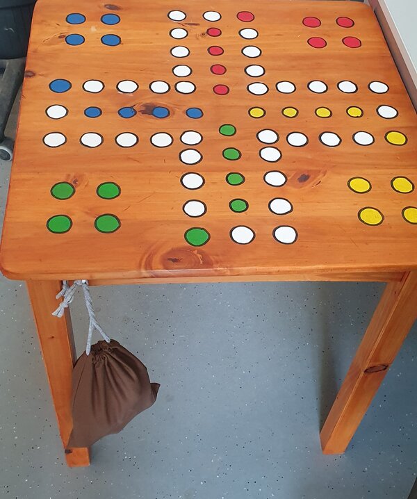 Zu sehen ist ein Holztisch, auf dem ein Mensch Ärgere dich nicht Spielfeld aufgemalt ist.