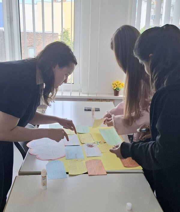 Drei weibliche Teilnehmerinnen beugen sich über einen Tisch, auf dem viele bunte Moderationskarten ausliegen. 
