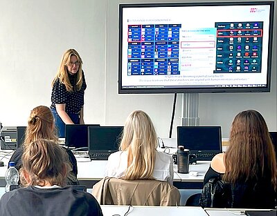 Mit KI zu barrierefreier Bildung – Teil 2 Workshopleiterin steht vorn im Klassenraum und referiert vor Schülerinnen und Schülern über Künstliche Intelligenz.