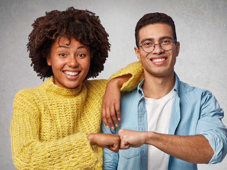 Eine schwarzhaarige junge Frau und ein schwarzhaariger junger Man strecken sich die Faust gegeneinander (Bro Fist')