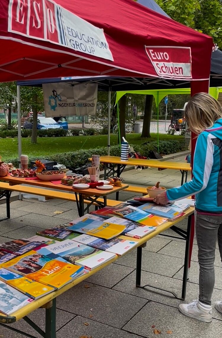 Eine Interessentin in hellblauer Trainingsjacke, hellen Sneakern und grauer Jeans schaut sich Informationsmaterial am Euro-Schulen-Stand an.