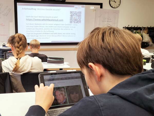 Auf die Wand vorne in einem Klassenzimmer wird ein Bild mit Verhaltenspunkten bei Fake News projiziert.