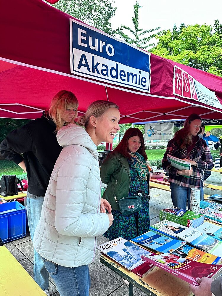 Vier engagierte Mitarbeiterinnen stehen am Stand der Euro-Schulen und Euro Akademie. Eine Mitarbeiterin spricht lächelnd zu Interessierten, die auf dem Foto nicht zu sehen sind. 