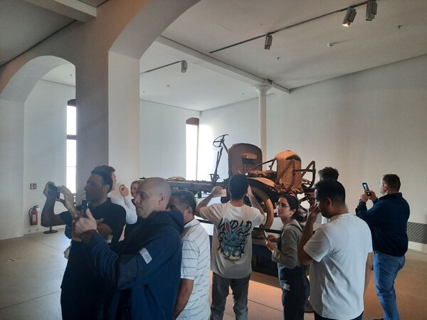 Eine Gruppe von Menschen steht in einem Museum und betrachtet ein altes Militärfahrzeug. Einige Personen machen Fotos, während andere das Exponat betrachten.