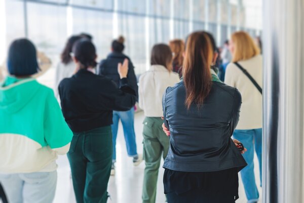 Junge Menschen stehen mit dem Rücken zur Kamera und schauen sich in einem Raum um.
