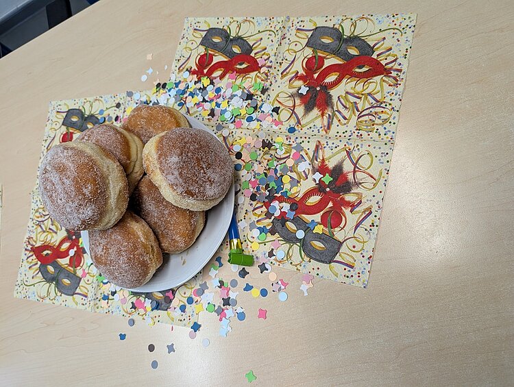 Ein voller Gebäck-Teller mit Berlinern auf einem geschmückten Tisch mit buntem Konfetti und Karnevalsservietten. Das Foto spiegelt die fröhliche Stimmung zum Fasching am 11.11.2025 um 11:11 Uhr.  