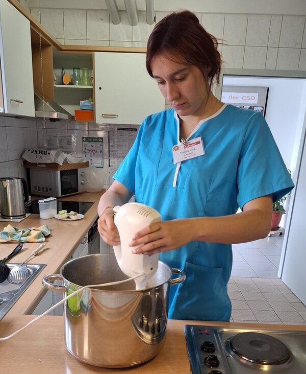 Eine Auszubildende steht in türkiser Schütze in der Lehrküche der Euro-Schulen Hoyerswerda und püriert das zubereitete Apfelmus im Topf.