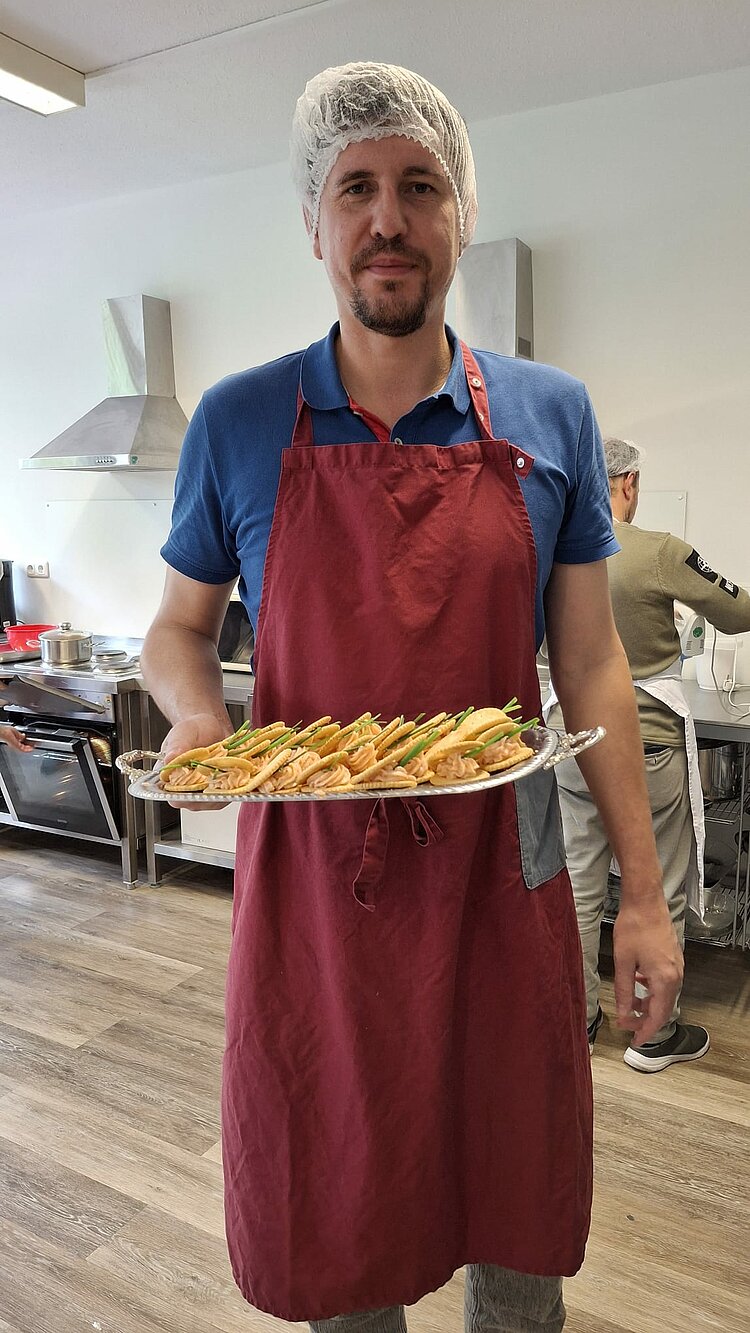 Ein Teilnehmer mit Kochhaube und Schürze präsentiert stolz ein Tablett mit kulinarischen Köstlichkeiten.
