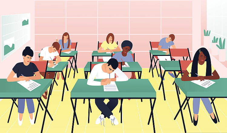Zu sehen ist ein Klassenraum mit mehreren in Reihen aufgestellten grünen Tischen, an denen Schülerinnen und Schüler mit unterschiedlichen Aussehen und Hautfarbe sitzen und eine Prüfung schreiben.