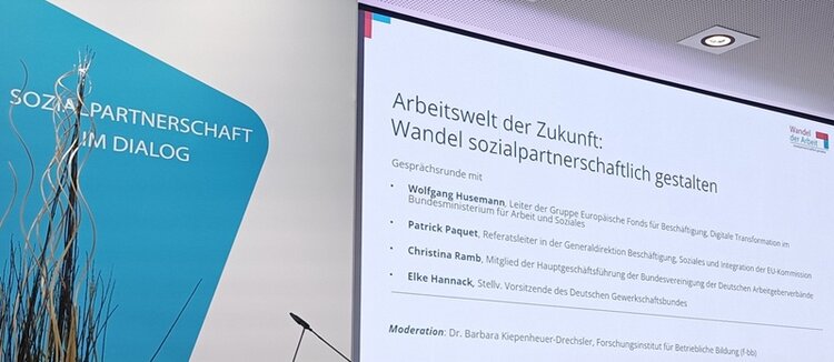 Im Hintergrund ist eine Leinwand mit Informationen zur Veranstaltung.