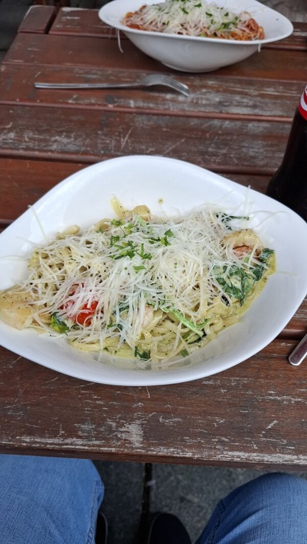 Leckere Pasta mit Spinat, Tomaten und Parmesan wird draußen auf einem Holztisch serviert – ein wohlverdienter kulinarischer Abschluss des Ausflugs.