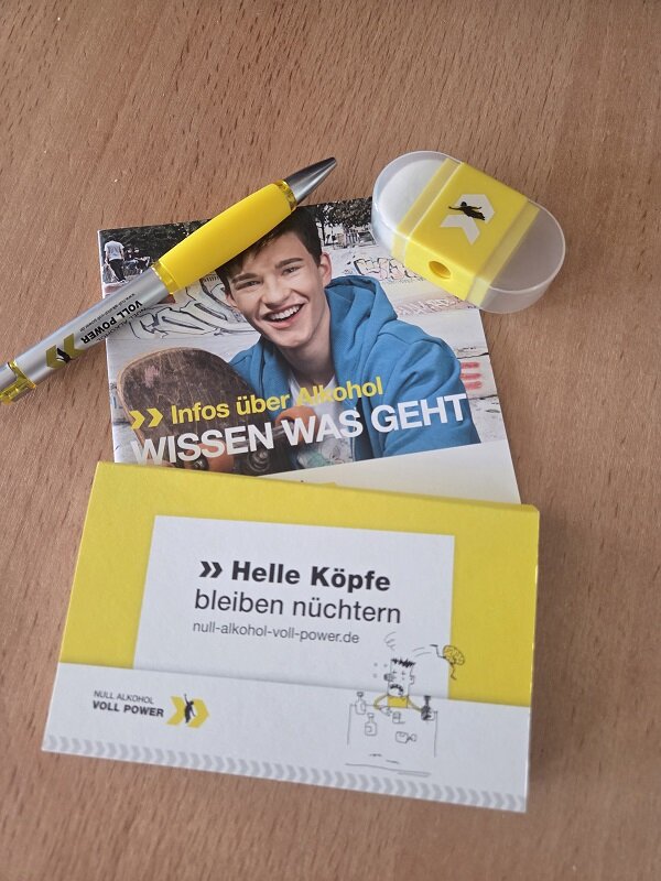 Auf einem Tisch liegen Informationsmaterialien der Kampagne "Null Alkohol – Voll Power". Zu sehen sind ein gelber Kugelschreiber, ein Radiergummi und Flyer mit Aufschriften wie "Infos über Alkohol – WISSEN WAS GEHT" und "Helle Köpfe bleiben nüchtern".