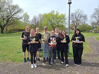 Die angehenden Verkäuferinnen und Verkäufer der Euro-Schulen Hoyerswerda posieren draußen auf einer Wiese mit Schokoosterhasen und Osterbasteleien in den Händen, gut gelaunt für ein Gruppenbild.