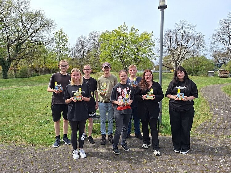 Die angehenden Verkäuferinnen und Verkäufer der Euro-Schulen Hoyerswerda posieren draußen auf einer Wiese mit Schokoosterhasen und Osterbasteleien in den Händen, gut gelaunt für ein Gruppenbild.