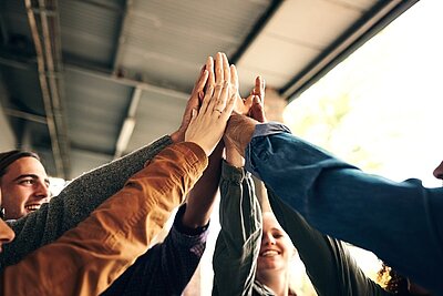 Ihr Weg zur Mittleren Reife – Gemeinsam zum Erfolg! Glückliche Schülerinnen und Schüler stehen im Kreis und heben ihre Hände zum High Five. Sie freuen sich über ihren Erfolg im Vorbereitungskurs zum Mittleren Bildungsabschluss an den Euro-Schulen Wiesbaden.
