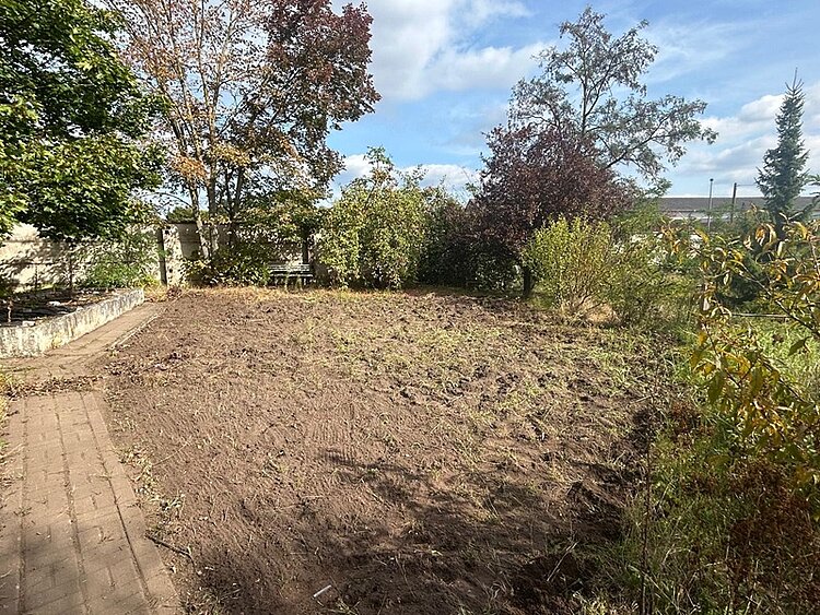 Blick in den Garten und auf ein umgepflügtes Feld- und Wiesenstück.