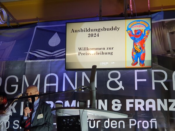 Ein Bühne mit grauem Rednerpult und ein Bildschirm im Hintergrund mit der Aufschrift Ausbildungsbuddy 2024.