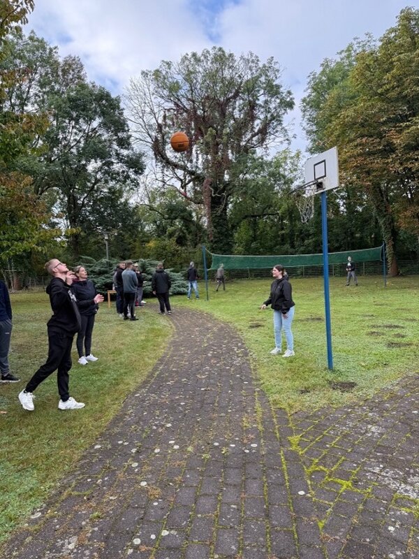 Eine Gruppe Auszubildender spielt Basketball und Volleyball auf einem Sportplatz im Freien.