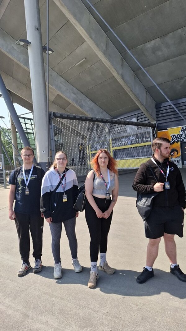 Die Gruppe steht vor dem Eingangsbereich des Rudolf-Harbig-Stadions; alle tragen Besucherausweise um den Hals und genießen die sonnige Atmosphäre.
